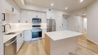 Located at 1337 E Woodland Ave in Millcreek, Utah, this thoughtfully designed one-bedroom, one-bathroom unit offers a clean, contemporary aesthetic throughout its single-floor layout. Light hardwood flooring flows seamlessly across every room, complementing the bright white walls and recessed lighting that keep the space feeling open and airy.

The heart of the home is a well-appointed open-concept kitchen, dining, and living area. The kitchen features tall white shaker cabinets, a subway tile backsplash, a white quartz countertop, and a warm wood-toned island with built-in drawers — an ideal prep and gathering space. Stainless steel appliances, including a refrigerator, range, microwave, and dishwasher, complete the modern kitchen package.

The living area benefits from large, black-framed windows that invite natural light and provide views of the surrounding building exterior. A glass-panel door leads to a private balcony, extending the living space outdoors.

The bedroom is a serene retreat with a spacious walk-in closet and additional closet storage, all finished in the same neutral palette. The bathroom is clean and functional, featuring a wood-toned vanity with a white countertop, built-in shelving, and a full tub-shower combination with white tile surround. A dedicated laundry area and utility room round out this efficiently designed, move-in-ready home.