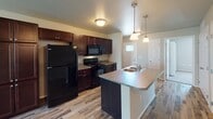 This single-floor residence in Sioux Falls, South Dakota offers a well-organized layout with a thoughtful mix of flooring and functional design throughout. The kitchen serves as a central highlight, featuring rich dark wood cabinetry, black appliances including a refrigerator, range, and microwave, and a central island with an integrated sink and laminate countertop. Pendant lighting above the island adds a decorative touch, while wood-look flooring extends through the kitchen and into the adjoining living area, creating a cohesive open feel.

The living space transitions from hard flooring to carpet and includes a sliding glass door fitted with vertical blinds, providing outdoor access and natural light. Multiple bedrooms are carpeted and finished with neutral-toned walls, flush-mount ceiling lighting, and windows that bring in daylight. Each room offers a clean, versatile space suitable for various uses.

Two bathrooms serve the unit, one featuring a tub-shower combination with a dark wood vanity and wood-look flooring, and another with a stand-alone shower stall, a navy vanity with a countertop sink, and a lighted mirror. Both bathrooms are finished with consistent, practical fixtures throughout.