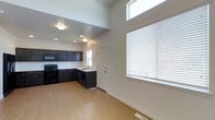 This thoughtfully designed multi-story space spans three floors, offering a versatile and functional layout throughout. The main living area immediately impresses with its dramatic soaring ceilings, which create an expansive, airy atmosphere that feels open and welcoming. Large windows, including a striking clerestory window positioned high on the wall, flood the interior with natural light, enhancing the bright, clean aesthetic of the neutral white walls.

The kitchen is a standout feature, outfitted with rich, dark espresso-toned cabinetry that provides a bold contrast against the light surroundings. It is equipped with black appliances, including a range and overhead microwave, and a stainless steel sink set beneath a window. The L-shaped cabinetry configuration maximizes storage and counter space, making it both practical and visually striking.

Underfoot, warm light hardwood flooring flows seamlessly through the main level, adding a natural, inviting quality to the space. Recessed lighting supplements the abundant natural light, ensuring the area is well-lit at any time of day. A interior door off the kitchen area provides convenient access to additional spaces. Together, the high ceilings, generous windows, quality finishes, and cohesive design make this a compelling and functional multi-level space.