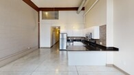 Located at 1900 E Superior Ave in Cleveland, Ohio, this two-story loft-style unit showcases an industrial character blended with modern finishes. The main level offers a generous open-plan layout with polished concrete tile flooring, dramatically high ceilings, and exposed ductwork that reinforce the building's industrial heritage. Original brick surrounds large arched windows, flooding the space with natural light while offering views of the surrounding neighborhood. Structural wood beams accent the upper portions of the walls, adding warmth to the otherwise contemporary aesthetic.

The kitchen is well-appointed with white cabinetry, dark granite countertops, a mosaic tile backsplash, and stainless steel appliances including a refrigerator, range, and microwave. A peninsula provides additional counter space and casual seating potential. A hallway connects to the full bathroom, which features a tub/shower combination accented by decorative mosaic tile. Two closets offer practical storage solutions on the main level.

A staircase leads to the upper loft level, where sloped ceilings, soft carpeting, and industrial-style pendant lighting create a cozy, intimate atmosphere. A large interior clerestory window overlooks the main living area below, maintaining visual connectivity between the two floors. The loft also includes additional closet space, completing this characterful urban retreat.