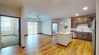 Located at 1850 Summerfield Way in Sun Prairie, Wisconsin, this single-floor unit offers a thoughtfully designed open-concept layout that seamlessly connects the living, dining, and kitchen areas. Warm-toned luxury vinyl plank flooring extends throughout the main living spaces, complemented by crisp white walls and dark wood baseboards that add a clean, modern contrast.

The kitchen is a standout feature, outfitted with rich, dark wood cabinetry, a white quartz countertop, a subway tile backsplash, and a full suite of stainless steel appliances including a refrigerator, range, microwave, and dishwasher. A central island with pendant lighting above provides additional prep space and a casual dining area. The open living room benefits from a tray ceiling with a ceiling fan and a large sliding glass door that fills the space with natural light and provides outdoor access.

The bedrooms are carpeted for comfort, offering a quiet retreat from the main living areas. The bathrooms feature white vanities with quartz countertops, framed mirrors, and the same wood-look flooring found throughout. A dedicated in-unit laundry space houses a stacked washer and dryer along with shelving for additional storage. The layout is efficient and well-organized, making excellent use of every area.