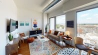 Located at 1900 Half St SW in Washington, DC, this single-floor residence showcases a contemporary industrial-chic aesthetic that blends modern finishes with urban character. The open-concept layout connects the living and kitchen areas seamlessly, creating a bright and functional living space. Exposed silver ductwork runs along the ceiling, serving as a striking architectural feature that complements the hardwood floors found throughout the main living areas.

The kitchen is well-appointed with stainless steel appliances, including a gas range, microwave, and refrigerator, all set against a dark subway tile backsplash. Warm wood upper cabinetry is paired with sleek gray lower cabinets and dark countertops, striking a balance between warmth and modern design. Large windows in the living area invite abundant natural light and offer open views of the Washington, DC cityscape, enhancing the airy feel of the space.

The bedroom is a calm, neutral retreat with soft gray tones and carpet flooring, providing a comfortable contrast to the hardwood in the main living areas. The bathroom features gray brick-style tile walls surrounding a full soaking tub and shower combination, complemented by large-format floor tiles and dark vanity storage, offering a clean and refined finish throughout.