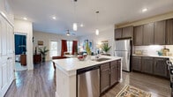 Located at Champions Gate in San Antonio, TX, this one-bedroom, one-bathroom residence offers a thoughtfully designed open-concept layout that seamlessly connects the kitchen and living room. The kitchen is a standout feature, showcasing rich taupe shaker-style cabinetry, quartz countertops, a classic subway tile backsplash with under-cabinet lighting, and a full suite of stainless steel appliances including a refrigerator, range, microwave, and dishwasher. A central island with an integrated sink provides additional prep space and casual dining potential. Wood-look flooring flows throughout the main living areas, lending warmth and continuity to the space. The living room is bright and inviting, with large windows allowing generous natural light and a ceiling fan overhead. The bedroom offers plush carpeting, a ceiling fan, and a sizable window that fills the room with natural light, complemented by a dedicated closet for storage. The bathroom is clean and functional, featuring wood-look flooring and a shower/tub combination. Recessed lighting and neutral wall tones create a cohesive, modern ambiance throughout this efficiently designed and well-finished San Antonio residence.