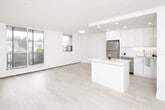 Located at 55 Tindale Court in Hamilton, Ontario, this single-floor unit presents a clean, contemporary design defined by an all-white palette and light wood-toned flooring that runs consistently throughout the space. The open-concept layout seamlessly connects the living area to the kitchen, creating a sense of openness and ease of movement.

The kitchen is a standout feature, outfitted with high-gloss white cabinetry extending to the ceiling, a full suite of stainless steel appliances including a refrigerator, stove, built-in microwave, and dishwasher, as well as a subway tile backsplash and a centrally positioned island with a clean white countertop. Recessed lighting illuminates the kitchen efficiently.

The living and bedroom areas are bright and airy, benefiting from large floor-to-ceiling sliding glass doors and oversized windows that invite natural light and provide views of the surrounding neighbourhood. Baseboard heating runs along the exterior walls beneath the windows. At least one bedroom includes a walk-in closet with a built-in rod and shelving system.

The overall ambiance is minimal and modern, with a neutral, light-filled aesthetic that offers a versatile, move-in-ready canvas.