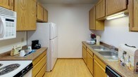 Located at 3100 33rd St S in Fargo, North Dakota, this single-floor unit offers a practical and well-organized layout. The galley-style kitchen is outfitted with warm oak cabinetry on both sides, providing ample storage and counter space, along with hardwood-style flooring that adds a clean, polished look. A double sink and full appliance setup make it a fully functional cooking space.

The hallway connects the main living areas to the bedrooms and bathroom, featuring the same light hardwood-style flooring and a vaulted ceiling section that adds a sense of openness. Multiple doors along the corridor lead to closets and additional rooms, keeping the layout organized and accessible.

The bedrooms are carpeted and feature vertical blinds over large windows that allow natural light to pour in, offering views of the surrounding neighborhood's tree lines. Baseboard heaters are present beneath the windows, ensuring warmth during Fargo's cold winters. A wall-mounted air conditioning unit in one bedroom provides climate control year-round.

The full bathroom includes a single vanity with a wide mirror, a toilet, and a tub-shower combination, finished with tile flooring for easy maintenance. Neutral tones and a textured ceiling are consistent throughout the unit, giving the space a cohesive and understated aesthetic well-suited for comfortable everyday living.