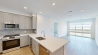 Located at 2000 Schindler Drive in South Amboy, NJ, this thoughtfully designed residence offers three bedrooms and two bathrooms across a single floor. The open-concept kitchen and living area serves as the heart of the home, featuring gray shaker-style cabinetry, a herringbone tile backsplash, quartz countertops, stainless steel appliances including a gas range and built-in microwave, and a central island with an undermount sink. Light wood-tone flooring flows throughout, lending warmth and continuity to the space. The living area is bright and airy, with large windows that frame scenic outdoor views and provide generous natural light. The spacious primary bedroom continues the clean, modern aesthetic with ample room and large windows overlooking the landscape. Additional bedrooms are well-proportioned, each offering closet storage with built-in shelving and rods. The bathrooms are finished with large-format tile flooring, wood-toned vanity cabinetry, white quartz countertops, and glass-enclosed showers. A dedicated laundry area houses a stacked GE washer and dryer unit alongside a Rinnai tankless water heater. The overall design is clean, contemporary, and move-in ready.