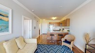 Located at 814 N 3rd St in Wilmington, NC, this single-floor residence offers a thoughtfully designed layout that balances comfort and functionality. The open-concept living and kitchen area serves as the heart of the home, where warm hardwood-style flooring flows throughout. The kitchen is well-equipped with stainless steel appliances — including a refrigerator, range, and built-in microwave — complemented by rich wood cabinetry, a tile backsplash, and a peninsula with bar seating that creates a natural gathering space. The adjacent living area accommodates relaxed seating and is anchored by a bold chevron-patterned area rug that adds a pop of coastal character. The bedrooms offer plush carpeting underfoot, with one room featuring a ceiling fan, natural light from a window with shutters, and a warm, restful ambiance. A secondary bedroom provides a more intimate setting with direct sightlines to the main living space. The bathroom presents a clean, tile-floored design with a vanity, mirror, and shower. Crown molding details and neutral wall tones throughout create a cohesive, polished look. This residence is well-suited for those seeking a comfortable, move-in-ready home in the heart of Wilmington.