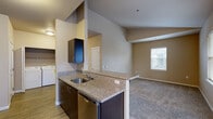 This single-floor, 2-bedroom, 2-bathroom unit offers a practical and well-appointed layout. The kitchen is equipped with stainless steel appliances, including a range, microwave, refrigerator, and dishwasher, complemented by granite-style countertops and dark espresso cabinetry. A peninsula counter connects the kitchen to the combined dining area, which transitions into the carpeted living room. The living area features notably vaulted ceilings, enhancing the sense of openness, and receives natural light through a window with blinds. An in-unit washer and dryer are conveniently located adjacent to the kitchen.

The primary bedroom offers vaulted ceilings, a window, and a dedicated closet, with an en-suite bathroom featuring a stand-up shower and tile flooring. The second bedroom is carpeted, benefits from dual windows providing ample natural light, and includes a closet with built-in shelving. An additional hallway bathroom serves the second bedroom. Flooring throughout alternates between wood-look planks in the kitchen and hallways, and carpet in the living and bedroom areas. Neutral warm-beige tones are consistent throughout the unit.