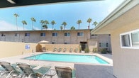 Located at 3131 Cauby St in San Diego, this outdoor pool amenity space offers a well-appointed recreational retreat designed for comfort and relaxation. The centerpiece is a generously sized rectangular swimming pool with crystal-clear blue water, surrounded by a wide concrete pool deck lined with lounge chairs perfect for sunbathing beneath the Southern California sun. Towering palm trees frame the backdrop, enhancing the resort-like atmosphere.

A covered patio area adjoins the pool deck, featuring exposed beam ceilings with a classic, clean white finish and built-in overhead lighting. This shaded space is furnished with a round glass-top dining table and comfortable cushioned chairs, offering a comfortable area to gather out of direct sunlight. The covered patio also provides direct sightlines to the pool, making it ideal for both relaxation and socializing.

A dedicated BBQ station is available on the patio, equipped with multiple stainless steel grills set against a stucco wall — well-suited for outdoor entertaining. A drinking fountain is conveniently mounted along the exterior wall near the pool. The entire space is enclosed by perimeter walls that provide privacy while maintaining an open, airy feel. The single-level layout ensures easy accessibility throughout the entire outdoor area.