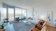 Located at 8800 Lombard in San Diego, this model unit showcases a thoughtfully designed single-level layout with a clean, contemporary aesthetic throughout. The interior is characterized by light wood flooring, soft neutral walls, and an abundance of natural light that flows freely through floor-to-ceiling sliding glass doors.

The living area is generously proportioned, featuring direct access to a private balcony that frames sweeping views of the surrounding treetops and San Diego cityscape. The open, airy atmosphere is enhanced by carefully curated furnishings and curated wall art, reinforcing the unit's modern sensibility.

The kitchen is outfitted with light wood cabinetry featuring sleek hardware, stainless steel appliances including a gas range and built-in microwave, and ample counter and storage space. The layout is efficient and well-organized, suited for both everyday cooking and entertaining.

The bedroom continues the unit's light, serene palette, with large sliding glass doors opening to the balcony, offering the same impressive outdoor views. A tufted upholstered headboard and soft accent pillows contribute to the room's tranquil character.

The bathroom is a standout feature, centered around a frameless glass-enclosed shower clad in large-format stone tiles, complemented by LED-lit mirrors and polished fixtures, lending a distinctly spa-like quality to the space.
