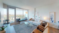 Located at 8800 Lombard in San Diego, this model unit showcases a thoughtfully designed single-level layout with a clean, contemporary aesthetic throughout. The interior is characterized by light wood flooring, soft neutral walls, and an abundance of natural light that flows freely through floor-to-ceiling sliding glass doors.

The living area is generously proportioned, featuring direct access to a private balcony that frames sweeping views of the surrounding treetops and San Diego cityscape. The open, airy atmosphere is enhanced by carefully curated furnishings and curated wall art, reinforcing the unit's modern sensibility.

The kitchen is outfitted with light wood cabinetry featuring sleek hardware, stainless steel appliances including a gas range and built-in microwave, and ample counter and storage space. The layout is efficient and well-organized, suited for both everyday cooking and entertaining.

The bedroom continues the unit's light, serene palette, with large sliding glass doors opening to the balcony, offering the same impressive outdoor views. A tufted upholstered headboard and soft accent pillows contribute to the room's tranquil character.

The bathroom is a standout feature, centered around a frameless glass-enclosed shower clad in large-format stone tiles, complemented by LED-lit mirrors and polished fixtures, lending a distinctly spa-like quality to the space.