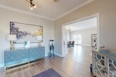 Located at 9245 Cuandet Rd in Gulfport, Mississippi, this single-story community clubhouse — known as Bayou Landing — offers a thoughtfully designed, open-concept interior that balances functionality with modern style. The space is finished throughout with warm-toned hardwood-style flooring and crisp crown molding, creating a cohesive and polished aesthetic.

Visitors are welcomed through a bright foyer entry featuring glass-paneled French doors that fill the space with natural light. A stylish teal and gold credenza, complementary artwork, and mid-century modern light fixtures set the tone upon arrival. Adjacent to the entry is a dedicated office or leasing area, providing a professional yet approachable workspace.

The expansive main gathering area flows seamlessly between a lounge and dining zone. The lounge is anchored by comfortable seating arranged around a wood-and-metal coffee table, while a striking sputnik chandelier adds a contemporary focal point overhead. The dining area features a large farmhouse-style table surrounded by mixed metal and leather chairs, illuminated by a matching sputnik fixture. Multiple sets of French doors line the perimeter, offering abundant natural light and easy outdoor access.

A kitchenette at the rear of the space includes grey cabinetry, a peninsula counter, and standard appliances, supporting events and gatherings. Throughout, the design balances modern industrial touches with warm, inviting finishes.