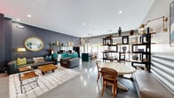 Located at 310 N Malcolm X Blvd in Dallas, TX, this single-floor space offers a thoughtfully designed open-plan layout with a distinctly eclectic and artistic character. Polished concrete floors run throughout, lending an industrial-chic aesthetic that anchors the space's contemporary design. Large floor-to-ceiling windows along one wall flood the interior with natural light while offering views of the surrounding greenery, creating an airy and expansive atmosphere.

The main living area is generously proportioned and organized into several defined zones. A bold teal kitchen island with bar seating and pendant globe lighting serves as a focal point near the window wall, accompanied by a stainless steel refrigerator. A cozy nook features a mint-green channel-tufted banquette, a round marble-top dining table, and open shelving displaying curated décor and books.

The lounge area is furnished with rich blue wingback chairs, a leather accent chair, and plush area rugs, creating an inviting gathering space. A striking neon sign and dark accent wall near the elevator add a dramatic, artistic touch. Colorful original artwork is displayed throughout, contributing to the space's vibrant, gallery-like ambiance. A doorway leads to an additional room visible in the background, extending the functional layout further.
