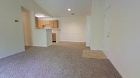 This single-floor residential space offers a clean, functional layout centered around an open-concept living area that flows seamlessly into the kitchen. The living space is finished with wall-to-wall carpeting in a neutral tone, creating a comfortable and cohesive feel underfoot, while a tiled entry area near the front door provides a practical transition zone.

The kitchen is positioned along one side of the space and features a raised pass-through bar that separates it from the main living area without sacrificing the open feel. Light wood cabinetry lines the upper walls, offering ample storage, while under-counter space adds further utility. Recessed and fluorescent lighting ensures the kitchen is well-lit and functional.

The walls throughout are painted in a soft, neutral tone that keeps the interior feeling bright and airy. Recessed lighting in the ceiling supplements the natural ambiance, maintaining a welcoming atmosphere. The layout is straightforward and practical, making efficient use of the available space. An interior door on one side provides access to additional areas of the unit. Overall, the space presents a tidy, move-in-ready environment with a simple, understated aesthetic well-suited for everyday living.
