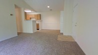 This single-floor residential space offers a clean, functional layout centered around an open-concept living area that flows seamlessly into the kitchen. The living space is finished with wall-to-wall carpeting in a neutral tone, creating a comfortable and cohesive feel underfoot, while a tiled entry area near the front door provides a practical transition zone.

The kitchen is positioned along one side of the space and features a raised pass-through bar that separates it from the main living area without sacrificing the open feel. Light wood cabinetry lines the upper walls, offering ample storage, while under-counter space adds further utility. Recessed and fluorescent lighting ensures the kitchen is well-lit and functional.

The walls throughout are painted in a soft, neutral tone that keeps the interior feeling bright and airy. Recessed lighting in the ceiling supplements the natural ambiance, maintaining a welcoming atmosphere. The layout is straightforward and practical, making efficient use of the available space. An interior door on one side provides access to additional areas of the unit. Overall, the space presents a tidy, move-in-ready environment with a simple, understated aesthetic well-suited for everyday living.