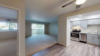 Located at 1105 W Olive Ave in Sunnyvale, California, this single-story unit offers a practical and well-organized layout. The living area is generously proportioned, finished with plush carpeting and neutral-toned walls that create a calm, inviting atmosphere. A full-width sliding glass door fitted with vertical blinds allows abundant natural light to fill the space while providing direct access to an outdoor area and views of surrounding greenery.

The kitchen is thoughtfully designed with a recessed ceiling that adds subtle architectural definition. It features gray cabinetry with contemporary hardware, white quartz countertops, a stainless steel refrigerator, electric range, and dishwasher, all set atop light wood-style flooring that extends throughout the non-carpeted areas of the unit.

The bathroom includes a wide vanity with a white countertop, undermount sink, gray cabinetry, and a mirrored medicine cabinet, offering ample storage and a clean, modern aesthetic. Additional rooms feature soft carpeting, neutral walls, and good natural light. A ceiling fan is present in the main living area, contributing to year-round comfort. The overall design is understated and functional, well-suited for everyday living in the heart of Sunnyvale.