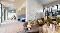 Located at 4335 W Fourth St in Reno, Nevada, this thoughtfully designed single-floor amenity space blends contemporary aesthetics with natural, mountain-inspired elements. The layout accommodates a variety of functions, from casual socializing to focused work, making it a versatile and welcoming environment throughout.

The lounge area serves as a visual centerpiece, anchored by a sweeping hand-painted mountain mural rendered in soft blue-gray tones that evokes the Sierra Nevada landscape. Seating here includes leather armchairs with brass-frame accents, a sculptural live-edge wood coffee table, and plush green accent chairs, all arranged on layered area rugs over light wood-tone flooring. An adjacent semi-private booth seating nook with upholstered gray panels provides a quieter retreat within the open space.

A fully equipped kitchen features a bold navy island with a white countertop and tan leather bar stools, complemented by light wood cabinetry, open shelving, a stainless steel range with hood, and a geometric tile backsplash. A large-format refrigerator anchors one wall, and the open-plan layout connects seamlessly to a bright lounge area with floor-to-ceiling windows offering views of the surrounding neighborhood. Natural light flows generously throughout, enhancing the space's warm, modern ambiance.