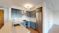 This single-floor unit offers a thoughtfully designed layout with a cohesive aesthetic carried throughout. The kitchen stands as a highlight of the space, showcasing two-toned gray shaker cabinetry — deeper slate uppers paired with softer blue-gray lowers — complemented by white subway tile backsplash, light quartz countertops, and stainless steel appliances including a gas range and refrigerator. A undermount sink and pendant-style flush mount lighting complete the polished look.

The open living area extends from the kitchen, featuring warm wood-look flooring that runs continuously through the space, white walls, and large windows fitted with roller shades that invite natural light and street views. The layout flows naturally between the living and sleeping areas, with the bedrooms offering a clean, neutral palette, ample space, and decorative flush mount fixtures overhead. One bedroom features a walk-in closet and a sizable window overlooking the surrounding neighborhood.

The bathroom is finished with white subway tile surrounding a soaking tub and shower combination, accented by a mosaic border detail, while charcoal hexagonal floor tile adds visual contrast. The overall ambiance is modern yet warm, with consistent finishes creating a unified and comfortable living environment.