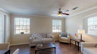 This two-floor residence offers a thoughtfully arranged layout with 2 bedrooms and 2 bathrooms across a comfortable footprint. The living room features rich hardwood-style flooring, crown molding, a ceiling fan with light fixture, and multiple windows that fill the space with natural light and neighborhood views. An arched architectural detail adds a refined touch to the living area. Adjacent to the living room, the dining area accommodates a four-person table and benefits from additional window light and door access, creating a bright and functional space for everyday meals. The kitchen is equipped with white cabinetry, laminate countertops, and black appliances including a refrigerator, range, and microwave. A dedicated in-unit laundry room with washer and dryer hookups is conveniently located just off the kitchen. Both bedrooms are carpeted and well-lit, each featuring ceiling fans and ample closet space. The two bathrooms include tiled floors, tub-shower combinations, vanities with storage cabinetry, and warm lighting. The attached garage offers a clean concrete floor, overhead door opener, and built-in overhead storage rails, providing practical additional storage and parking. Overall, the space presents a warm, neutral palette throughout.