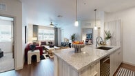 Located in Gilbert, Arizona, this single-story 2-bedroom, 2-bathroom home offers a thoughtfully designed open-concept layout that maximizes every square foot. The kitchen serves as a centerpiece, featuring a large granite-topped island with bar seating, light wood cabinetry, stainless steel appliances, a tile backsplash, and elegant pendant lighting — all flowing seamlessly into the living area. The living room is bright and inviting, with wide windows dressed in floor-length drapes that fill the space with natural light, complemented by wood-look flooring and a ceiling fan overhead. Both bedrooms are carpeted and well-proportioned, each with large windows offering outdoor views and dedicated closet space. The primary bathroom features a glass-enclosed shower and a vanity with stone countertops, while the secondary bathroom offers a full soaking tub with tile surround. An in-unit stacked washer and dryer adds everyday convenience. Throughout the home, a cohesive neutral palette with clean white walls creates a bright, modern ambiance well-suited to the sunny Gilbert, AZ environment.