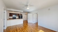 This well-appointed 2-bedroom, 1-bathroom unit offers a thoughtfully designed layout with a clean, modern aesthetic throughout. Warm hardwood-style flooring flows seamlessly across the entire space, complementing the bright white walls and creating a cohesive, inviting atmosphere.

The open-concept kitchen and living area serves as the heart of the unit. The kitchen is outfitted with dark walnut-toned cabinetry, light quartz-style countertops, a central island with a double-basin sink and dishwasher, and a full suite of black stainless appliances including a refrigerator, range, and over-the-range microwave. Large floor-to-ceiling windows and sliding glass doors lead to a private balcony, flooding the living area with abundant natural light and providing views of the surrounding building exterior.

Both bedrooms are comfortably sized, each featuring ceiling fans and generous natural light. The primary bedroom includes access to a dedicated closet. A second closet provides additional storage elsewhere in the unit.

The bathroom is finished with the same wood-style flooring, a single-sink vanity with dark cabinetry, and a clean, minimal design with accessibility-friendly grab bars. The unit is part of a multi-story residential building with modern exterior architecture and landscaped common areas visible from the windows.