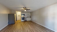 This single-floor unit offers a clean, modern design with an open-concept layout that seamlessly connects the living area and kitchen. Light-toned, wood-look flooring extends throughout the space, contributing to a bright and cohesive aesthetic. The living area is generously sized, featuring a ceiling fan with integrated lighting, a textured ceiling, and large windows with blinds that allow ample natural light to fill the room. A door provides direct exterior access from the living space.

The kitchen is efficiently designed and well-equipped with a full suite of stainless steel appliances, including a refrigerator, electric range, over-the-range microwave, and dishwasher. White shaker-style cabinetry and a classic white subway tile backsplash complement the dark countertops, giving the kitchen a fresh, contemporary look. A single-basin sink with a modern faucet completes the functional workspace.

Adjacent to the kitchen, a walk-in closet provides generous storage. The bathroom is clean and well-maintained, featuring white cabinetry with brushed nickel hardware, a single-sink vanity with a light countertop, a full tub-shower combination with white tile surround, and matching wood-look flooring that ties the space together. The overall ambiance of the unit is neutral, light, and move-in ready.