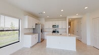 Located at 2101 E Landings Way in Port Charlotte, Florida, this two-story home presents a clean, contemporary design with a bright, neutral palette maintained throughout both levels. The open-concept main floor is anchored by a well-appointed kitchen featuring white shaker-style cabinetry, light stone countertops, stainless steel appliances including a French door refrigerator, electric range, and built-in microwave, and a central island with an undermount double sink. Large-format tile flooring extends through the kitchen and living areas, lending a cohesive, polished look. The living area opens directly to the outdoors through sliding glass doors, offering serene water views that bring a distinctly Florida feel to the interior. A bathroom on the lower level includes a single vanity with white cabinetry, a tub-shower combination with tile surround, and tile flooring. The upper level hosts multiple bedrooms, each carpeted and finished in crisp white, with windows that allow natural light and outdoor views. The home's consistent use of white finishes, recessed lighting, and clean architectural lines creates a bright, move-in-ready atmosphere suited to Florida living.