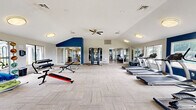 Located at 113 Magnolia Dr in Franklin, TN, this single-floor fitness center offers a generously sized, open exercise space designed to accommodate a comprehensive range of workout activities. The room features vaulted ceilings that enhance the sense of openness, complemented by multiple ceiling fans that promote airflow and comfort throughout. Large windows line the walls on multiple sides, flooding the interior with natural light while providing views of the surrounding greenery and outdoor areas.

The flooring throughout consists of durable, neutral-toned carpet tiles, providing a practical and comfortable surface for various exercises. A bold navy blue accent wall adds a striking visual contrast to the otherwise light and airy white walls, giving the space a modern, energetic aesthetic.

The facility is well-equipped with a diverse selection of cardio machines, including treadmills, ellipticals, stationary upright bikes, and spinning cycles. Strength and functional training options include a multi-station cable machine, a dumbbell rack, a weight bench, and a rowing machine. Additional fitness accessories such as stability balls and medicine balls round out the equipment offerings. Mirrored wall sections support form-checking during workouts. Glass doors connect to adjacent community spaces, and ample open floor space throughout allows for stretching and group exercise activities.