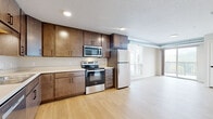 This 1-bedroom, 1-bathroom flat at Flats at Malcolm Yards in Minneapolis, MN offers a well-designed, single-floor layout with contemporary finishes throughout. Light hardwood-style flooring runs continuously across the living, kitchen, and bedroom areas, creating a cohesive and bright interior.

The kitchen is thoughtfully appointed with rich, dark wood cabinetry offering generous upper and lower storage, white countertops, a double-basin stainless steel sink, and a full suite of stainless steel appliances including an electric range, over-the-range microwave, refrigerator, and dishwasher. Recessed lighting illuminates the space effectively.

The open living area benefits from large windows and a sliding glass door that leads to a private balcony with outdoor views of the surrounding neighborhood. Exposed ductwork adds an industrial design accent to the living space.

The bedroom is a comfortable, well-lit room with a large window, a built-in closet with shelving, and direct access to the rest of the unit. The bathroom features a clean, minimalist design with light tile flooring, a soaking tub, and brushed nickel fixtures and hardware. An entry closet near the front door provides additional storage upon arrival.