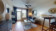 This single-floor residence offers a thoughtfully designed layout that balances comfort and functionality throughout. The living area serves as the heart of the home, featuring warm hardwood-style flooring, a ceiling fan, and large windows with a glass door that flood the space with natural light and provide outdoor views. The open, inviting atmosphere is further enhanced by neutral toned walls that complement the rich décor accents.

The kitchen is a standout feature, showcasing bold dark cabinetry, a tile backsplash, and granite-style countertops that extend into a breakfast bar — ideal for casual dining. Black appliances, including a refrigerator, range, and microwave, complete this well-equipped space.

The bedroom is generously sized and filled with natural light from large windows dressed in navy drapes. A ceiling fan adds comfort, and the hardwood-style floors carry throughout, maintaining a cohesive aesthetic.

The bathroom is finished with consistent attention to detail, featuring a granite-style vanity countertop with dark cabinetry, a full soaking tub with tile surround, and a large framed mirror. Recessed lighting adds a polished touch.

Overall, the space presents a warm, contemporary ambiance with a cohesive color palette of navy, grey, and warm wood tones throughout.