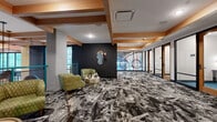 Located at 1015 N Alexander Street in Charlotte, NC, this single-floor amenity space delivers a bold, contemporary design identity across a generously sized layout. The space is unified by a dramatic, abstract-patterned carpet in black, white, and gray tones that creates a visually dynamic foundation throughout. Warm natural wood box beams accent the ceiling, contrasting beautifully with dark charcoal feature walls and bright, open sightlines.

The lounge area is anchored by a cluster of green tufted armchairs arranged around a gold metallic accent table, offering a welcoming and stylish gathering space. A sculptural, asymmetric mirror mounted on the dark wall adds an artistic focal point to this zone.

A glass-walled corridor leads to a series of private rooms framed by black metal and wood detailing, providing an open yet defined sense of separation. One room features a vibrant, full-wall graffiti-style mural with colorful character artwork, while others are equipped for focused work or meetings. Circular pendant light sculptures hang in the corridor, adding a distinctive artistic element.

A dedicated accent wall displays a curated collection of framed comic book covers, complemented by a checkered bench, reinforcing the space's eclectic, art-forward character. Abundant natural light filters through large windows, enhancing the overall energy of this thoughtfully designed amenity floor.