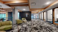 Located at 1015 N Alexander Street in Charlotte, NC, this single-floor amenity space delivers a bold, contemporary design identity across a generously sized layout. The space is unified by a dramatic, abstract-patterned carpet in black, white, and gray tones that creates a visually dynamic foundation throughout. Warm natural wood box beams accent the ceiling, contrasting beautifully with dark charcoal feature walls and bright, open sightlines.

The lounge area is anchored by a cluster of green tufted armchairs arranged around a gold metallic accent table, offering a welcoming and stylish gathering space. A sculptural, asymmetric mirror mounted on the dark wall adds an artistic focal point to this zone.

A glass-walled corridor leads to a series of private rooms framed by black metal and wood detailing, providing an open yet defined sense of separation. One room features a vibrant, full-wall graffiti-style mural with colorful character artwork, while others are equipped for focused work or meetings. Circular pendant light sculptures hang in the corridor, adding a distinctive artistic element.

A dedicated accent wall displays a curated collection of framed comic book covers, complemented by a checkered bench, reinforcing the space's eclectic, art-forward character. Abundant natural light filters through large windows, enhancing the overall energy of this thoughtfully designed amenity floor.