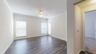 This single-floor residence offers a thoughtfully designed layout that balances comfort and functionality throughout. The spacious living area is a standout feature, showcasing rich, dark hardwood-style flooring that extends seamlessly through the main living spaces. Elegant crown molding lines the ceiling, adding a refined architectural touch, while a ceiling fan with integrated lighting provides both comfort and illumination. Multiple windows dressed with horizontal blinds flood the room with natural light, creating an open and airy atmosphere.

The galley-style kitchen is efficiently arranged with light wood cabinetry, dark granite-look countertops, and white appliances including a range, microwave, refrigerator, and dishwasher. The double-basin sink and ample cabinet storage make this kitchen as practical as it is functional. The flooring continues seamlessly from the living area into the kitchen.

The bathroom is clean and well-appointed, featuring a tub-shower combination, a toilet, and a single-sink vanity with white cabinetry and a large mirror overhead. The bedroom offers a comfortable, carpeted retreat with soft neutral tones and a generously sized window that invites natural light. The overall palette throughout the residence is warm and neutral, lending the space a cohesive and welcoming ambiance.