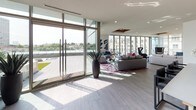 Located at 2902 Carlisle St in Dallas, TX, this single-floor club room is a sophisticated communal space designed with modern elegance and bold interior touches. Expansive floor-to-ceiling glass walls flood the interior with natural light while offering sweeping views of the surrounding cityscape and an adjoining outdoor terrace, creating a seamless indoor-outdoor connection.

The open-concept layout is anchored by two distinct lounge areas. The first features a curved sectional sofa adorned with vibrant teal and jewel-toned accent pillows, set against a striking damask-patterned feature wall with a mounted flat-screen television. The second lounge, positioned near the glass exterior wall, offers a contemporary sectional on a rich plum area rug, accented by bold abstract artwork and a glass side table, all bathed in abundant sunlight.

A well-appointed bar and kitchenette area serves as a central gathering point, showcasing a textured, scale-patterned dark accent wall, stainless steel appliances, and bar seating — ideal for social events and entertaining. Wood-look tile flooring runs throughout, providing a warm yet refined foundation that ties the spaces together.

Large sliding glass doors open directly to the terrace, where city views and outdoor amenities extend the usable space. The overall ambiance is vibrant, upscale, and inviting — a premium amenity space suited for both relaxed lounging and lively social gatherings.
