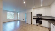 This single-floor residence at 8563 Litt Dr SE in Lacey, Washington, offers a clean, contemporary design throughout. The open-concept layout connects the living area and kitchen, creating a spacious, functional flow. Light hardwood-style flooring runs through the main living spaces, reflecting the recessed lighting overhead and contributing to a bright, airy atmosphere. Large windows fitted with vertical blinds allow natural light to fill the rooms while providing outdoor views of the surrounding neighborhood.

The kitchen is well-equipped with a full suite of stainless steel appliances, including a gas range, over-the-range microwave, dishwasher, and refrigerator. White cabinetry with dark countertops provides ample storage and workspace, complemented by open shelving for additional utility.

The bedrooms feature neutral carpet, ceiling fans, and windows that bring in natural light. The layout, visible in the floor plan, shows a well-organized arrangement of rooms with dedicated hallway access and closet space.

The bathroom includes a white vanity with dark countertop, a large mirror with overhead lighting, and a combination tub and shower. A secondary bathroom offers light hardwood-style flooring, a single-sink vanity, and a clean, minimal aesthetic consistent with the rest of the unit.