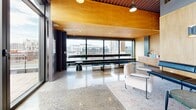 Located at 650 Wellington in Montréal's dynamic Griffintown neighbourhood, Chalet Urbain is a thoughtfully designed single-floor space that masterfully blends industrial character with refined modern aesthetics. The open-plan layout is anchored by striking polished terrazzo floors that reflect light beautifully throughout, while exposed wooden beam ceilings with corrugated metal detailing pay homage to the building's industrial roots and add warmth overhead. Visible ductwork and pendant lighting complement the loft-inspired atmosphere.

The space features a well-appointed communal area with marble-topped bar-height tables on casters, paired with sleek black metal stools, creating a versatile setting for gathering or collaborative work. A kitchenette with a sink and ample cabinetry supports the functional needs of the space. A lounge zone offers a more relaxed setting, furnished with a black leather bench, a plush bouclé armchair, and a light wood credenza set against clean birch plywood wall panels with designer sconce lighting.

Floor-to-ceiling glazed walls and sliding doors open onto a spacious outdoor terrace, flooding the interior with natural light and offering panoramic views of the Montréal skyline — a standout feature that seamlessly connects the indoors with the urban outdoors. This is a sophisticated, multi-functional urban space designed for comfort and style.