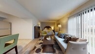 Located at 120 Montrose West Ave in Copley, Ohio, this single-floor studio unit offers a thoughtfully designed open-concept layout that seamlessly integrates the living and sleeping areas into one cohesive space. Light wood-style flooring flows throughout the main area, complemented by a textured ceiling and a neutral color palette accented with warm yellow tones. The living space features a comfortable sofa, a wood coffee table, and large windows with vertical blinds that allow ample natural light to fill the room. The sleeping area is set toward the back, furnished with a full bed, a tall dark wood dresser, and a cozy accent chair, creating a relaxed and functional atmosphere. A well-organized galley kitchen is equipped with gray cabinetry, dark countertops, stainless steel appliances including a range and dishwasher, and tile flooring for easy maintenance. The bathroom is a highlight of the unit, showcasing a wide granite-topped vanity with under-cabinet storage, a gold-framed mirror, and a separate tub-and-shower combination finished in clean white tile. The entry area provides a welcoming introduction to the space with additional natural light from side windows. Overall, this studio offers a practical and comfortable living environment in a well-maintained single-story setting.
