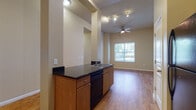 This well-appointed 3-bedroom, 3-bathroom single-floor residence offers a thoughtfully designed layout that balances open living spaces with private quarters. The heart of the home is an open-concept kitchen and living area, where a peninsula with dark granite-style countertops and a built-in sink and dishwasher anchors the space. The kitchen is fully equipped with black appliances including a refrigerator, range, and over-the-range microwave, complemented by warm wood cabinetry. Track lighting and a ceiling fan with light fixture serve the main living area, which benefits from soaring ceilings and a large window that invites abundant natural light and outdoor views. Hardwood-style flooring flows throughout the main living areas and hallways, lending warmth and cohesion. A dedicated hallway with a louvered utility door provides practical storage access. The bedrooms feature plush carpeting and generous windows, creating comfortable retreats. The bathrooms are clean and functional, each featuring wood-tone vanities with white countertops and tiled tub/shower combinations with chrome fixtures. A dedicated hallway connects the bedrooms, each with its own window view, completing this well-organized and bright residence.
