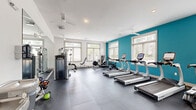 Located at 105 Ivy Green Way in Charleston, SC, this fitness center is a comprehensively outfitted exercise facility spread across a single floor. The space is divided into two distinct exercise rooms, together offering a full range of workout options for residents or members.

The main cardio and strength room is bright and spacious, featuring a bold teal accent wall that adds a vibrant energy to the clean, white interior. Multiple rows of True-brand treadmills and elliptical machines line the floor, complemented by a rowing machine, a cable weight machine, and a cable-based functional trainer. Large windows along the walls flood the room with natural light, while multiple ceiling fans ensure comfortable airflow. Durable interlocking rubber floor tiles and full-length mirrors round out the professional feel of this area.

The second exercise room serves as a dedicated free weights and functional training space. It is equipped with a full dumbbell rack, a BOSU balance trainer, a medicine ball and resistance band station, stability balls of varying sizes, and a yoga mat area. A wall-mounted flat-screen television and large mirror enhance the training experience. This room also benefits from natural light through its windows, creating an open and motivating environment. Together, the two rooms provide a thorough, gym-quality fitness experience.