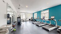 Located at 105 Ivy Green Way in Charleston, SC, this fitness center is a comprehensively outfitted exercise facility spread across a single floor. The space is divided into two distinct exercise rooms, together offering a full range of workout options for residents or members.

The main cardio and strength room is bright and spacious, featuring a bold teal accent wall that adds a vibrant energy to the clean, white interior. Multiple rows of True-brand treadmills and elliptical machines line the floor, complemented by a rowing machine, a cable weight machine, and a cable-based functional trainer. Large windows along the walls flood the room with natural light, while multiple ceiling fans ensure comfortable airflow. Durable interlocking rubber floor tiles and full-length mirrors round out the professional feel of this area.

The second exercise room serves as a dedicated free weights and functional training space. It is equipped with a full dumbbell rack, a BOSU balance trainer, a medicine ball and resistance band station, stability balls of varying sizes, and a yoga mat area. A wall-mounted flat-screen television and large mirror enhance the training experience. This room also benefits from natural light through its windows, creating an open and motivating environment. Together, the two rooms provide a thorough, gym-quality fitness experience.