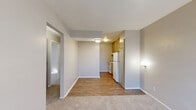 This two-bedroom, one-bathroom unit offers a practical and efficient single-floor layout designed to maximize functionality within a compact footprint. The combined kitchen and living area serves as the heart of the home, where light-toned hardwood-style flooring transitions seamlessly into carpeted living space. The kitchen is equipped with white appliances — including a refrigerator and range — paired with warm-toned cabinetry, while a window unit provides climate control in the living area. Natural light filters in through blinds-covered windows, lending a bright and airy feel throughout. A hallway connects the main living space to the private areas of the unit, leading to two carpeted bedrooms, each featuring neutral gray walls and dedicated closet space. The primary bedroom is a comfortable size, receiving natural light through a window. The second bedroom offers similar finishes and a bright atmosphere. The shared full bathroom is clean and straightforward, featuring a tiled tub-shower combination with a curtain and standard white fixtures. Textured ceilings are consistent throughout, and the overall color palette of soft grays and warm neutrals creates a calm, cohesive ambiance well-suited for everyday living.
