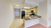 Located at 1215 E West Hwy in Silver Spring, Maryland, this single-floor residential unit offers a well-organized layout designed for comfortable everyday living. The kitchen is a functional highlight, featuring light maple cabinetry, dark granite countertops, tile flooring, and black appliances including a gas range, built-in microwave, refrigerator, and dishwasher. A skylight panel overhead brightens the workspace, while a peninsula counter with granite surface extends toward the living area, providing additional prep space and casual seating. The open sightline from the kitchen toward the entry hallway and living space creates a cohesive, connected flow throughout the unit. The living area is finished with wall-to-wall carpeting and neutral, light-toned walls that lend a clean and airy feel. A large window allows natural light to fill the room, offering views of the surrounding area. The bathroom is equipped with a vanity featuring warm wood cabinetry, a white countertop, a large mirror, tile flooring, and a shower-tub combination. Throughout the unit, the design emphasizes practicality and ease of use, with consistent neutral finishes that create a calm and welcoming atmosphere suited to a range of lifestyles.