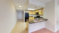 Located at 1215 E West Hwy in Silver Spring, Maryland, this single-floor residential unit offers a well-organized layout designed for comfortable everyday living. The kitchen is a functional highlight, featuring light maple cabinetry, dark granite countertops, tile flooring, and black appliances including a gas range, built-in microwave, refrigerator, and dishwasher. A skylight panel overhead brightens the workspace, while a peninsula counter with granite surface extends toward the living area, providing additional prep space and casual seating. The open sightline from the kitchen toward the entry hallway and living space creates a cohesive, connected flow throughout the unit. The living area is finished with wall-to-wall carpeting and neutral, light-toned walls that lend a clean and airy feel. A large window allows natural light to fill the room, offering views of the surrounding area. The bathroom is equipped with a vanity featuring warm wood cabinetry, a white countertop, a large mirror, tile flooring, and a shower-tub combination. Throughout the unit, the design emphasizes practicality and ease of use, with consistent neutral finishes that create a calm and welcoming atmosphere suited to a range of lifestyles.