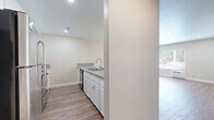 Located in the North Park neighborhood of San Diego, this one-bedroom, one-bathroom residence offers a thoughtfully designed layout with modern finishes throughout. Wood-look luxury vinyl flooring runs continuously across the entire space, creating a cohesive and clean aesthetic.

The combined kitchen and living area forms the heart of the home. The kitchen is well-equipped with white shaker-style cabinetry, grey speckled countertops, a mosaic tile backsplash, stainless steel appliances including a range and over-the-range microwave, and a black dishwasher. A peninsula with additional counter space separates the kitchen from the open living area, which is bathed in natural light from a large window and features a ceiling fan overhead.

The bedroom is a comfortable and private retreat with its own window offering views of surrounding greenery. The room connects to a hallway that leads to a closet area, providing practical storage. Double doors open from the bedroom into the hallway, enhancing the sense of flow.

The bathroom is well-appointed with white cabinetry, grey countertops, a full tub-shower combination, open built-in shelving, and wood-look flooring that ties in with the rest of the unit. Neutral tones throughout the space create a calm, welcoming ambiance ideal for comfortable everyday living.