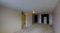 This single-floor space offers a straightforward and functional layout designed for comfortable everyday living. The main living area is generously sized, featuring a combination of light-toned carpet and tile flooring that defines distinct zones within the open floor plan. Neutral beige walls and a textured ceiling contribute to a clean, understated aesthetic throughout.

A built-in shelving unit provides convenient storage and display space, while a dedicated closet area with a dark-paneled door adds additional organizational capacity. The space flows naturally toward an entryway, reinforcing a sense of easy accessibility and movement.

An attached bathroom is visible from the main area, offering a practical and private layout. The bathroom features tile flooring and essential fixtures, positioned conveniently adjacent to the living and sleeping areas.

Overhead flush-mount lighting provides consistent illumination throughout the interior. The overall ambiance is calm and neutral, presenting a blank canvas that is well-suited for personalization. The single-level design ensures seamless navigation throughout the space, making it an accessible and efficient layout for a variety of uses.