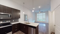 Located at 11501 W 81st St in Lenexa, Kansas, this contemporary single-floor residence showcases a thoughtfully designed open-concept layout that seamlessly connects the kitchen, dining, and living areas. The kitchen is a standout feature, equipped with rich dark espresso cabinetry, a striking quartz-topped island with a stainless steel undermount sink, pendant lighting, a textured tile backsplash, and a full suite of stainless steel appliances including a French door refrigerator, electric range, microwave, and dishwasher. The spacious living area benefits from soaring ceilings, a ceiling fan, and generous windows fitted with roller shades that invite abundant natural light while offering views of the surrounding greenery. A glass door provides access to a balcony, further enhancing the connection to the outdoors. Hardwood-style flooring flows throughout the main living spaces, while the bedrooms feature plush carpeting and ceiling fans. Each bedroom is well-lit with large windows and roller shades. The primary bathroom offers a dual-sink vanity with quartz countertops, dark cabinetry, a walk-in tiled shower with sliding glass doors, and hardwood-style flooring. The secondary bathroom mirrors the same refined aesthetic with a quartz vanity and a tiled tub-shower combination. This unit combines modern finishes with a clean, open design for a polished, comfortable living environment.
