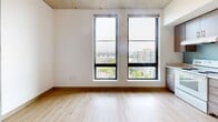 Located at 2045 SW River Pky in Portland, Oregon, this efficiently designed single-floor unit offers a well-planned layout that maximizes every square foot. The main living area features light hardwood flooring and crisp white walls, creating a clean, airy atmosphere. Two tall, floor-to-ceiling windows flood the space with natural light and frame impressive views of the Portland skyline and surrounding waterways, adding a striking sense of openness. An exposed concrete ceiling lends an industrial-modern character to the room.

The kitchen is outfitted with warm wood-toned cabinetry extending to the ceiling for ample storage, white appliances including a range, dishwasher, and refrigerator, and a light-toned countertop with a stainless steel sink. A soft blue tile backsplash adds a subtle pop of color, while an adjacent large window keeps the kitchen bright with natural light and city views.

Two bathrooms serve the unit, each finished with neutral tile flooring and clean white fixtures. The full bathroom includes a soaking tub and shower combination with a curved chrome curtain rod, complemented by warm-toned cabinetry. A separate entry area with light hardwood flooring and a built-in coat hook provides a functional transition into the living space.