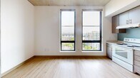 Located at 2045 SW River Pky in Portland, Oregon, this efficiently designed single-floor unit offers a well-planned layout that maximizes every square foot. The main living area features light hardwood flooring and crisp white walls, creating a clean, airy atmosphere. Two tall, floor-to-ceiling windows flood the space with natural light and frame impressive views of the Portland skyline and surrounding waterways, adding a striking sense of openness. An exposed concrete ceiling lends an industrial-modern character to the room.

The kitchen is outfitted with warm wood-toned cabinetry extending to the ceiling for ample storage, white appliances including a range, dishwasher, and refrigerator, and a light-toned countertop with a stainless steel sink. A soft blue tile backsplash adds a subtle pop of color, while an adjacent large window keeps the kitchen bright with natural light and city views.

Two bathrooms serve the unit, each finished with neutral tile flooring and clean white fixtures. The full bathroom includes a soaking tub and shower combination with a curved chrome curtain rod, complemented by warm-toned cabinetry. A separate entry area with light hardwood flooring and a built-in coat hook provides a functional transition into the living space.