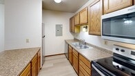 This single-floor unit offers a functional and straightforward layout across three bedrooms and two bathrooms. The living room serves as the central gathering space, featuring a brick fireplace with a wood mantel, a window providing natural light, plush carpeting, a textured ceiling, and a baseboard heating unit along the wall.

The kitchen is efficiently designed with warm honey-toned wood cabinetry, laminate countertops, and a peninsula that provides additional prep space and separates the kitchen from the adjoining area. Stainless steel appliances, including a range and microwave, are included, along with a double-basin sink and a built-in dishwasher. Light wood-look flooring runs throughout the kitchen and hallways.

The three bedrooms are carpeted and feature neutral walls, wood-trimmed windows, and baseboard heaters. The primary bedroom offers a generous footprint compared to the secondary rooms.

Both bathrooms include standard fixtures; one bathroom features a full tub-shower combination, while the other is conveniently situated near a stacked washer and dryer unit and features tile flooring and a vanity with a stone-look countertop. Closets are distributed throughout the unit, providing practical storage.