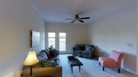 Georgetown Oaks is a single-floor residence that offers a welcoming and functional layout designed for comfortable everyday living. The living room serves as the heart of the space, featuring plush carpeted flooring that adds warmth underfoot. A ceiling fan is centrally positioned overhead, providing both practical airflow and a classic finishing touch to the room. Natural light fills the space through a set of double French doors that open onto a private balcony, creating a seamless connection between the interior and the outdoors. The doors are framed by clean white walls that keep the atmosphere bright and airy. The living area is generously proportioned, easily accommodating a full seating arrangement with multiple sofas and a central coffee table, making it ideal for both relaxing and entertaining. Crown molding along the upper walls adds a subtle architectural detail that elevates the overall aesthetic. The balcony beyond the French doors offers an outdoor extension of the living space, perfect for enjoying fresh air and surrounding views. Overall, Georgetown Oaks presents a tidy, light-filled residence with thoughtful design details and a comfortable, inviting ambiance throughout its single-level layout.
